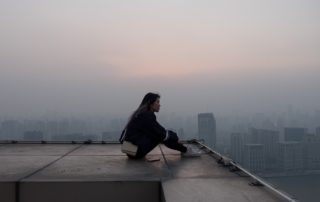 girl sitting to think on a roof top overlooking a city with buildings in the background