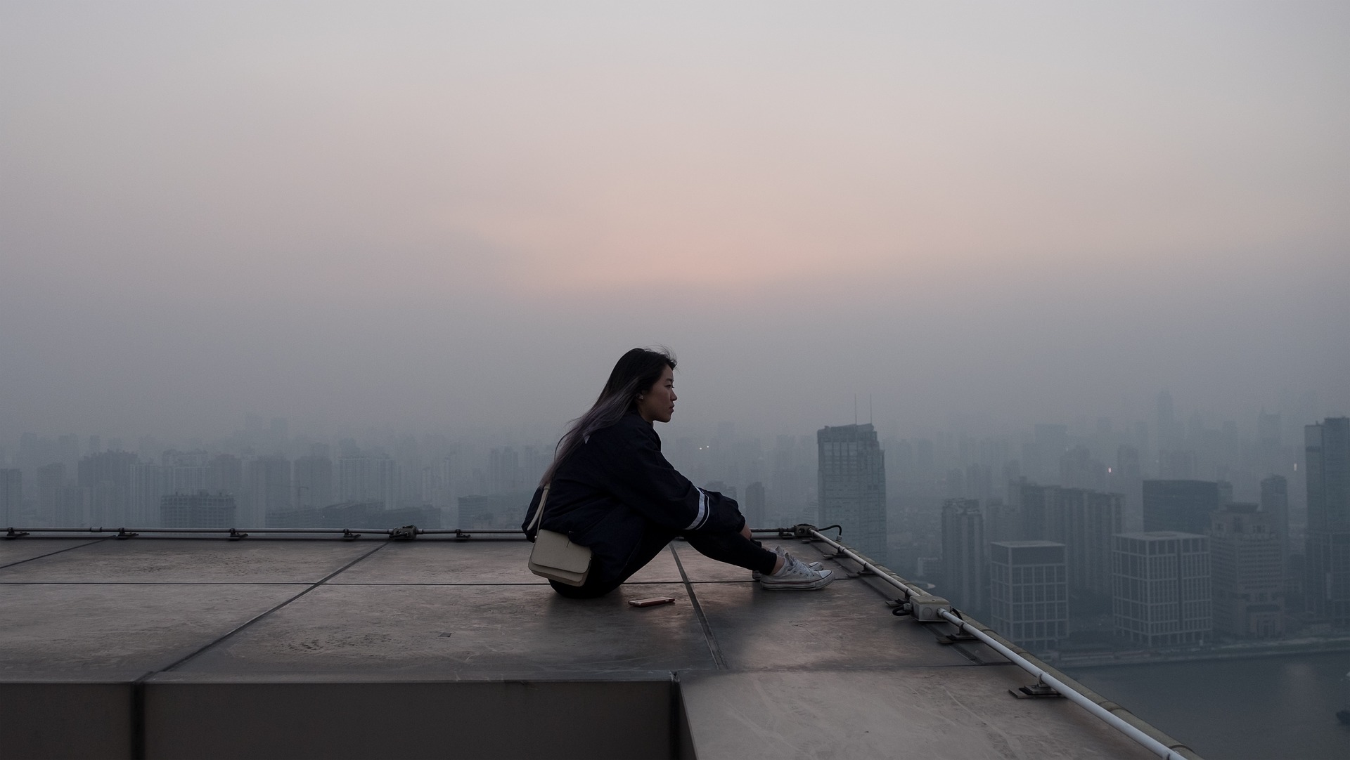 girl sitting to think on a roof top overlooking a city with buildings in the background