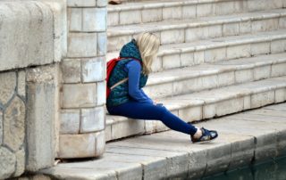 young woman sitting alone leaning against brick steps-anxiety