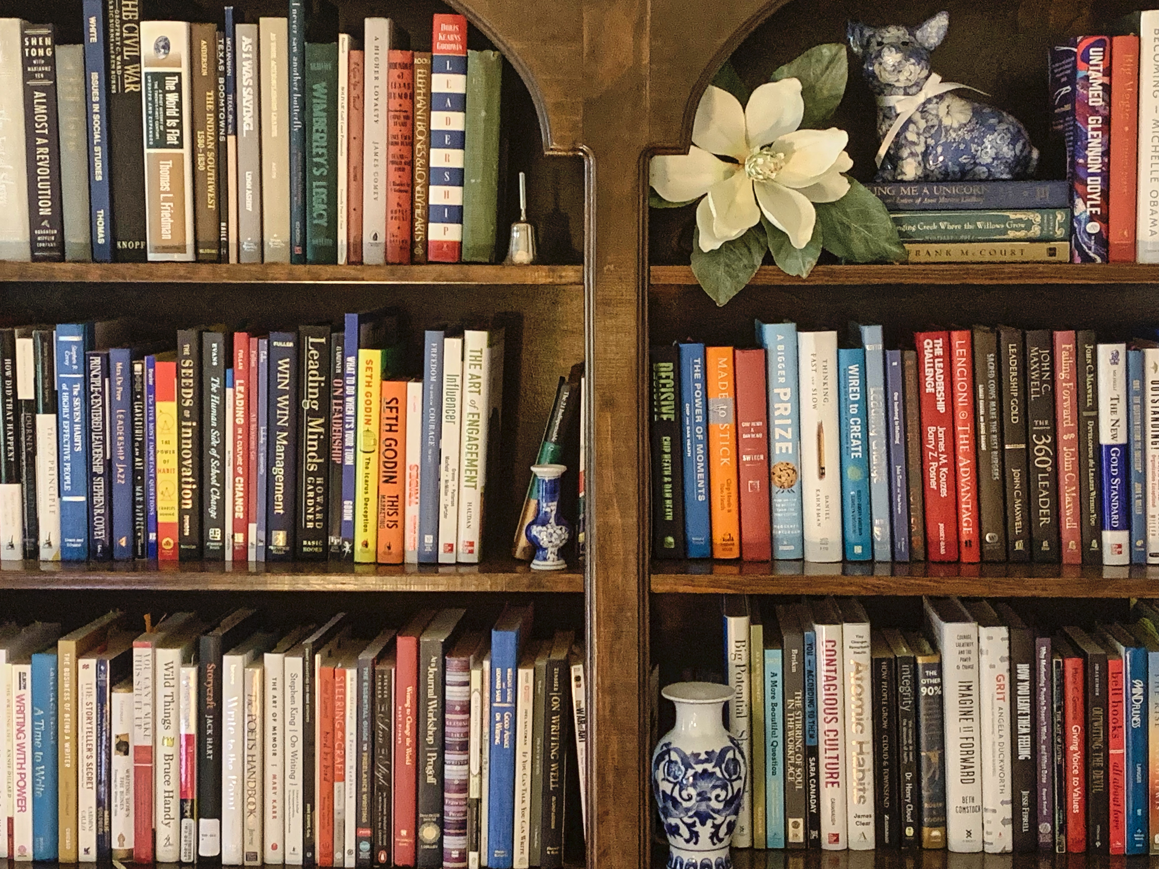 A bookshelf with books, vases, and a silk magnolia blossom-the start of a book list