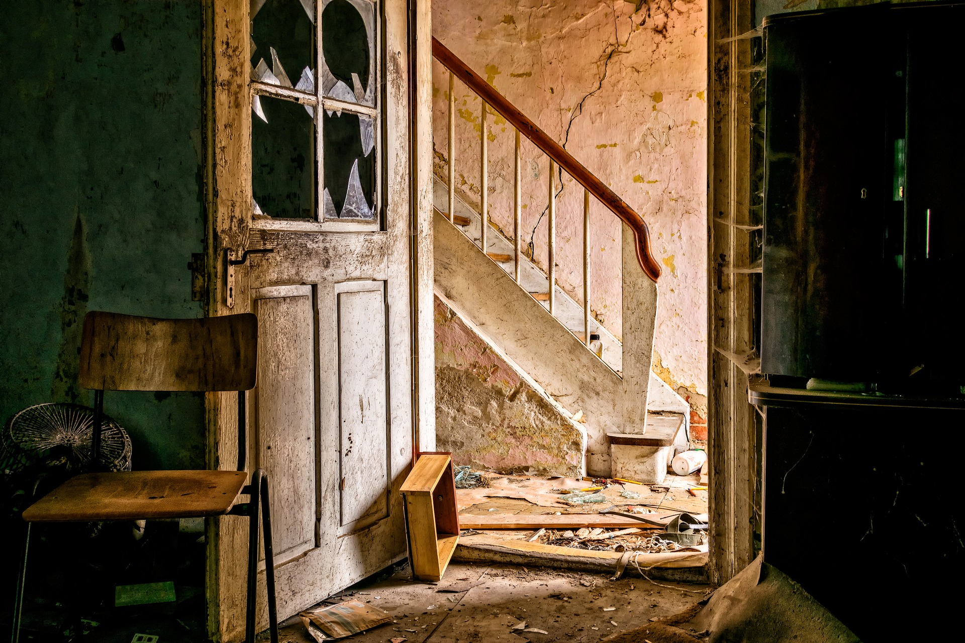an open door with broken panes and glass on the door with rubble with a stairway in the background-no there choice