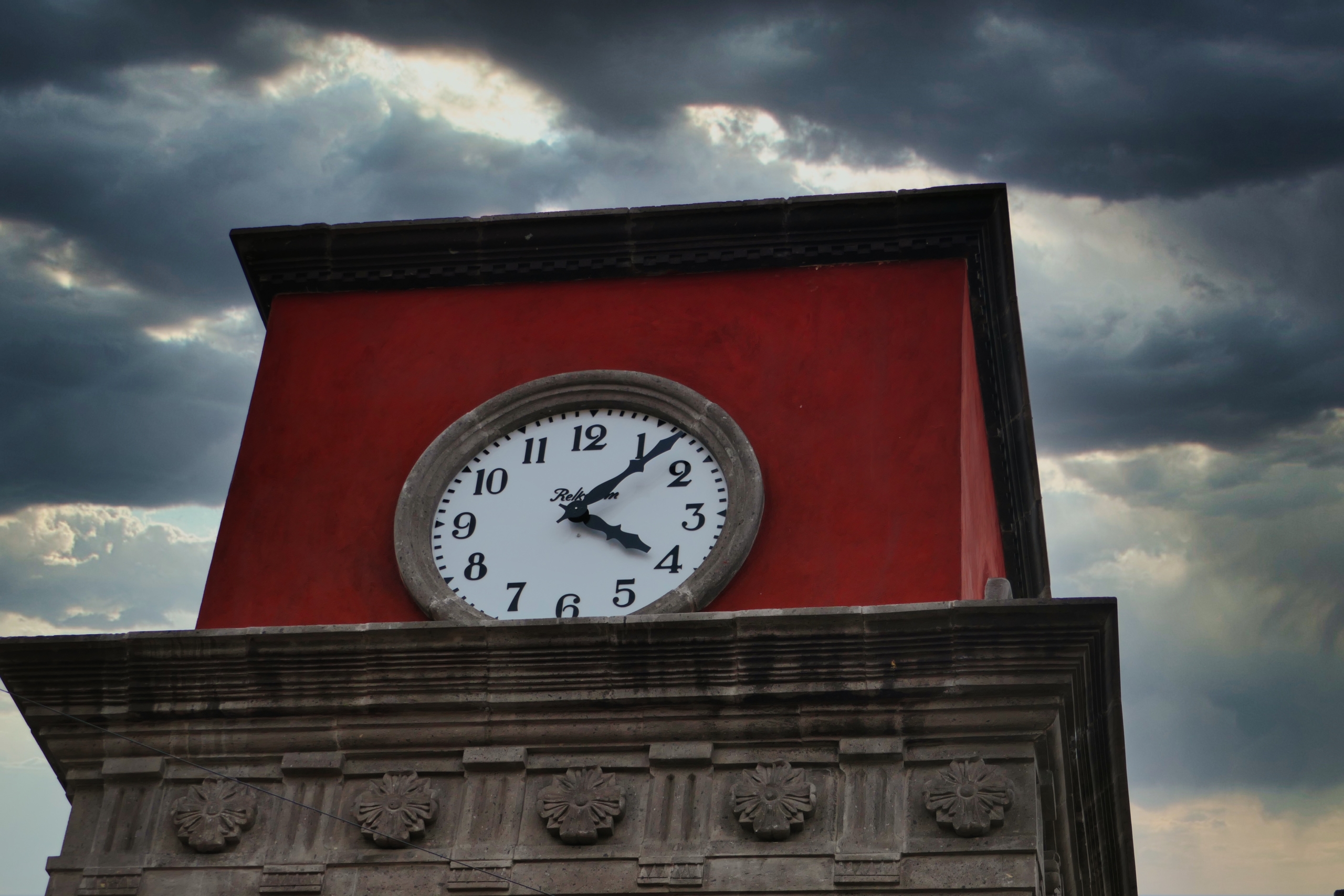 A clock on the red parapet of a building with stormy clouds in the sky-what's in a day?