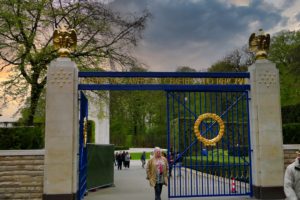 opened blue iron gate with gold wreath at the Luxembourg American Cemetery. A cloudy sky frames this door of remembrance