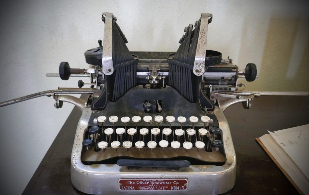 old manual typewritewr with white keys sitting on a table with an open book partially in view on the right-waiting for creativity