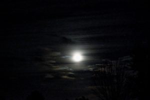 a full moon against a black sky with streaks of clouds visible in the darkened sky