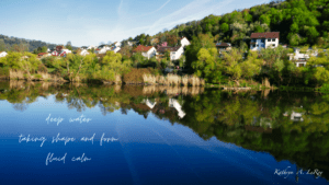 reflection of the village houses along the Main River with bright blue water and lighter blue sky with wispy white clouds