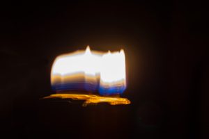 Abstract photograph of a candle flame with intentional camera movement it shows the blue then gold, then white of the flame; a golden aura surrounds the flame and creates a platform on which it sits
