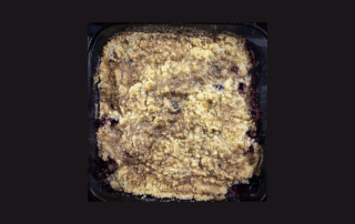 A dish of crusty blackberry cobbler against a black background
