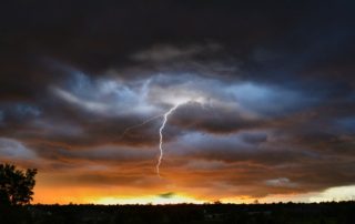 Dark storm clouds with the setting sun lighting the horizon and a lightening bolt flashing out of the dark clouds