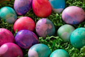 Dyed boiled eggs sitting an strips of paper grass, red, pink, green. purple swirls