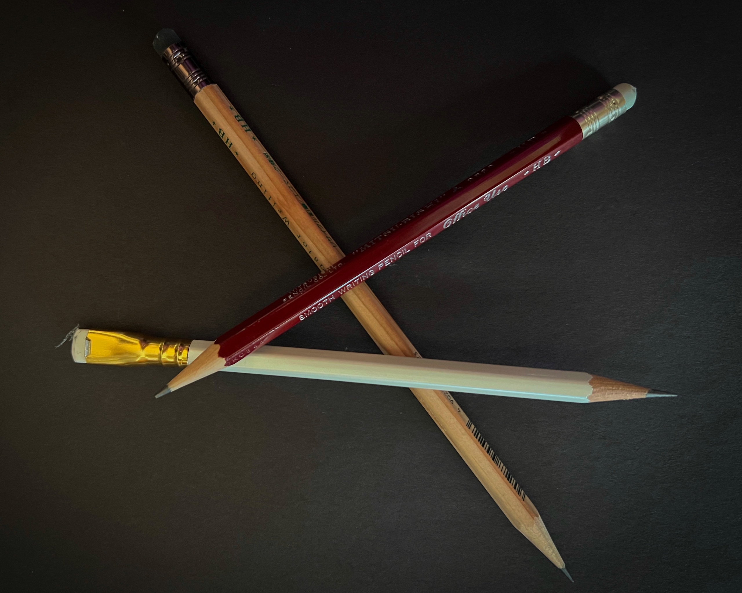 Three used pencils, red, white, and brown, laying at angles to one another on a black background