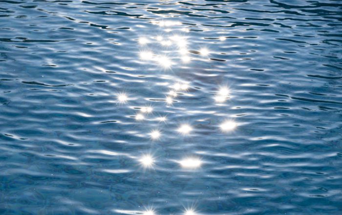 Sunlight glints across the blue water of a pool making multiple starbursts that appear to float in the air