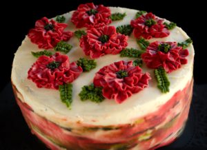 A beautifully decorated cake with vibrant red floral icing and green leaf accents atop a smooth white frosting surface.