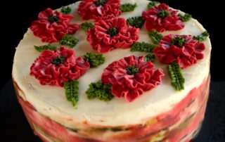 A beautifully decorated cake with vibrant red floral icing and green leaf accents atop a smooth white frosting surface.