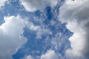 A bright blue sky filled with fluffy white clouds, some wispy, creating a serene and airy atmosphere.