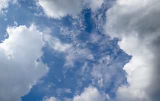 A bright blue sky filled with fluffy white clouds, some wispy, creating a serene and airy atmosphere.