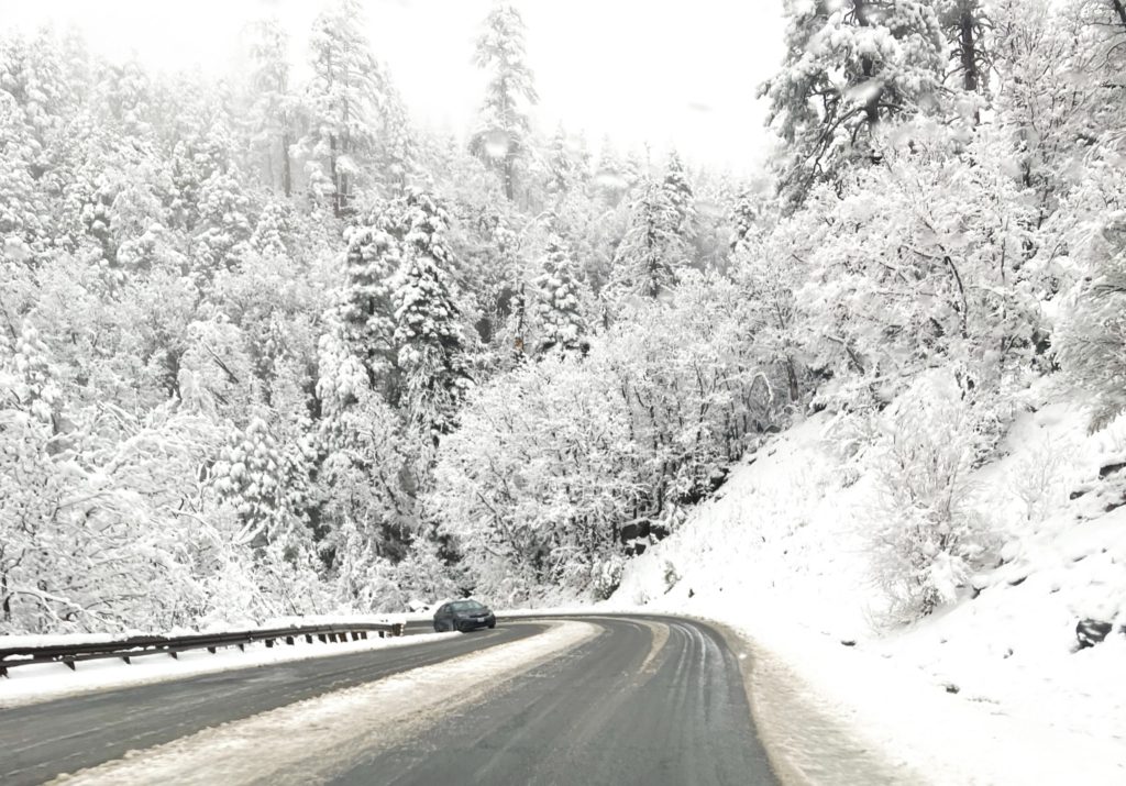 Unexpected Snow in May Unexpected Snow in May A winding road through dense, snow-covered trees in a serene winter landscape, with a single car navigating the snowy terrain