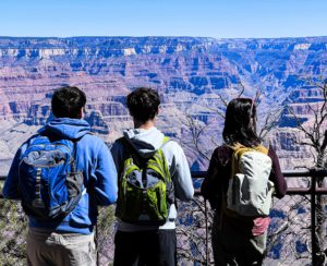 Three hikers, seen from behind, admire the vast landscape of the Grand Canyon under a clear blue sky.
