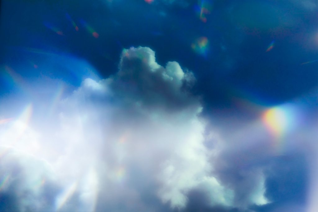 A vibrant blue sky with fluffy white clouds illuminated by sunlight, casting colorful reflections in the atmosphere.