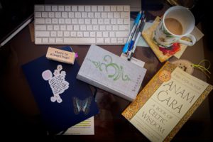 At Home © Kathryn LeRoy A workspace featuring a keyboard, notebooks, pens, a coffee cup, and a wooden block inscribed "there is always hope."