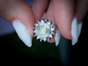 A close-up of a hand holding a decorative silver ring with purple gemstones, featuring a detailed star emblem at its center.