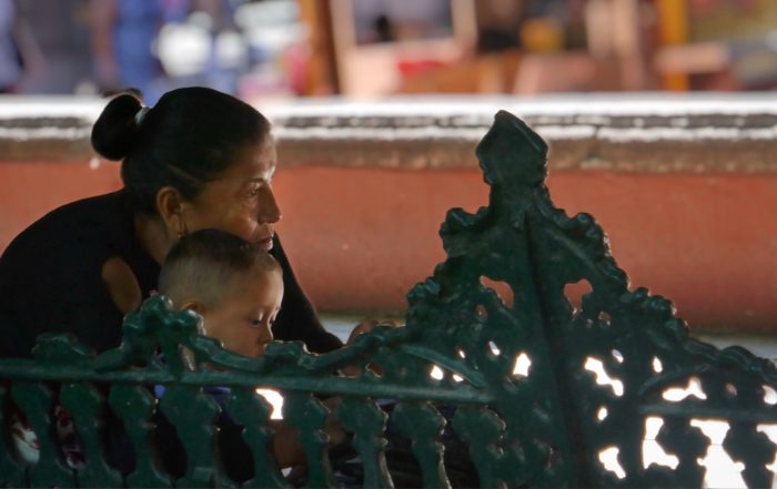 A person sitting on a bench, leaning over to care for a child, surrounded by a softly blurred background.