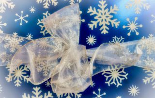 Elegant silver bow with snowflake patterns sits atop a blue background adorned with white snowflakes, evoking a festive, wintery mood.