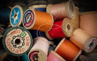 A collection of colorful sewing thread spools, stacked and scattered, featuring various brand labels and vibrant hues.