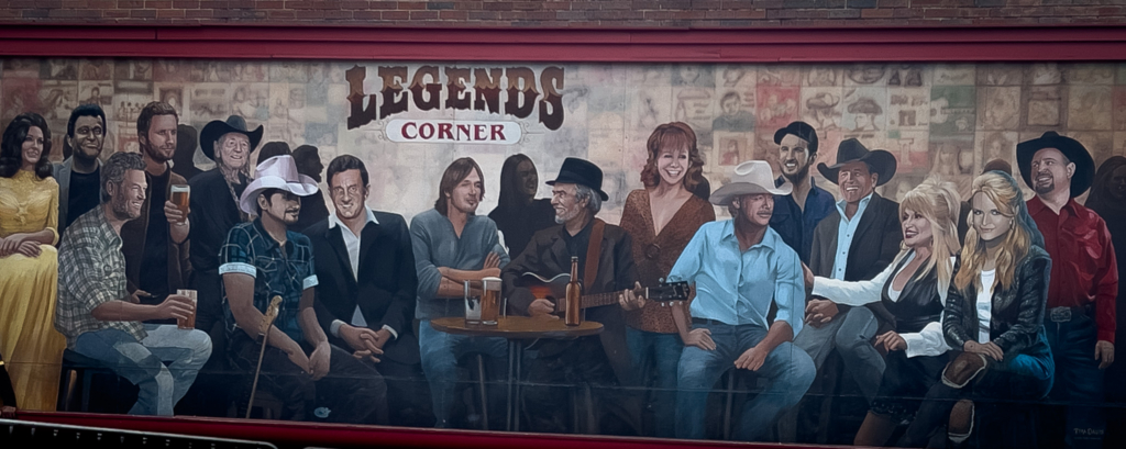 Mural titled 'Legends Corner' featuring a group of people in casual and cowboy attire with drinks and a guitar.
