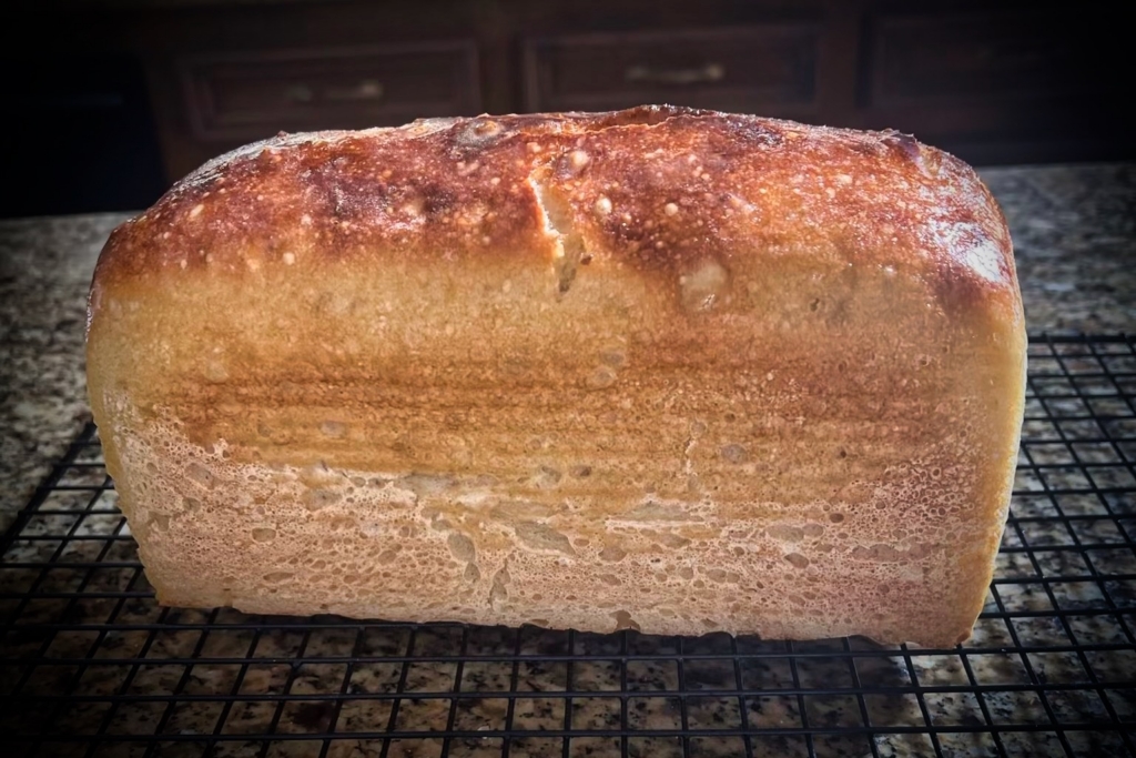 Loaf of golden-brown bread cooling on a wire rack on a kitchen countertop.