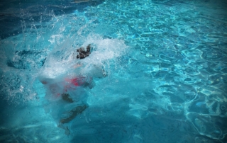 Person in red swimwear splashing into clear blue swimming pool water, creating large water splash and ripples.