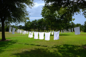 White clothes hanging on a clothesline between trees in a sunny, green open field under a partly cloudy sky.