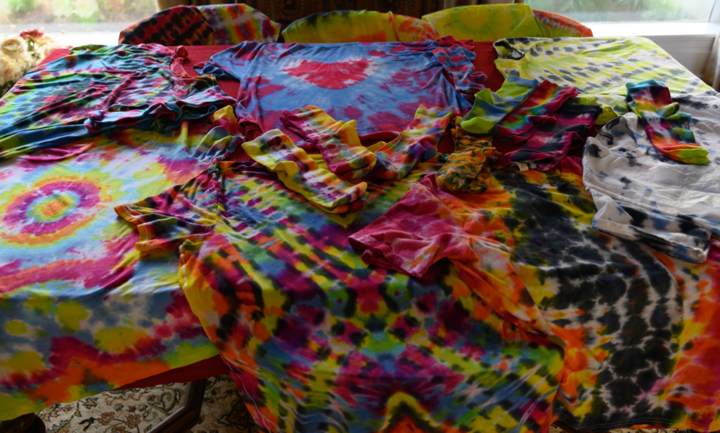 Colorful tie-dye T-shirts and matching socks laid out on a table in various bright patterns and rainbow hues.