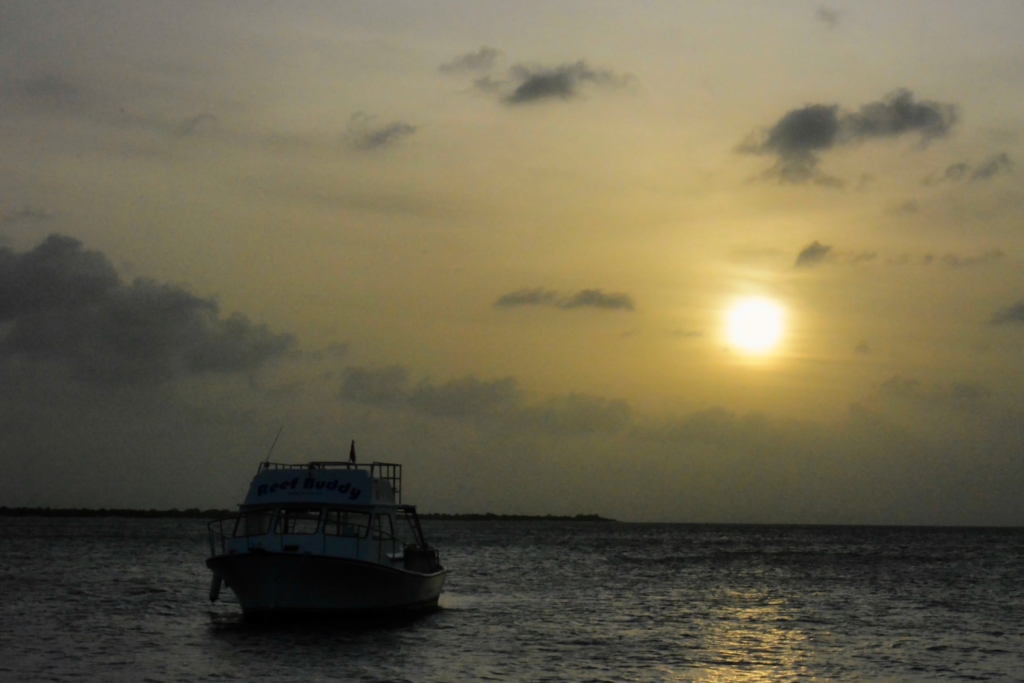 A small fishing boat silhouetted on rippling water beneath a cloudy golden sunset.