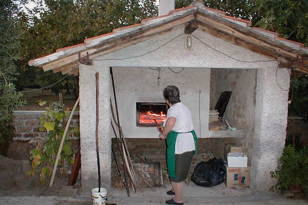 Person tending a wood-fired oven in a rustic outdoor kitchen.