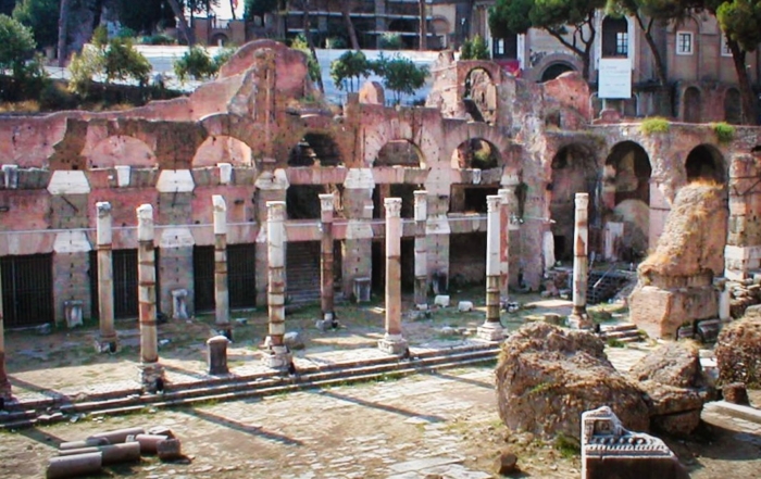 Ancient Roman ruins with weathered brick arches, marble columns, and scattered stone fragments in a sunlit archaeological site.